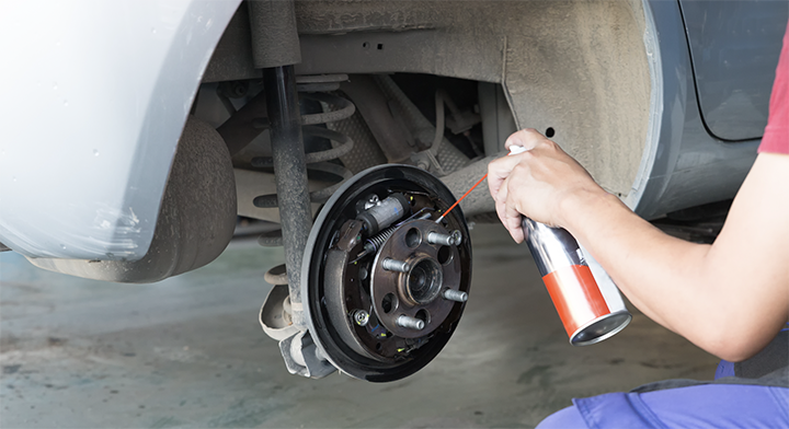 Person applying brake cleaner to a car’s brake assembly during maintenance.