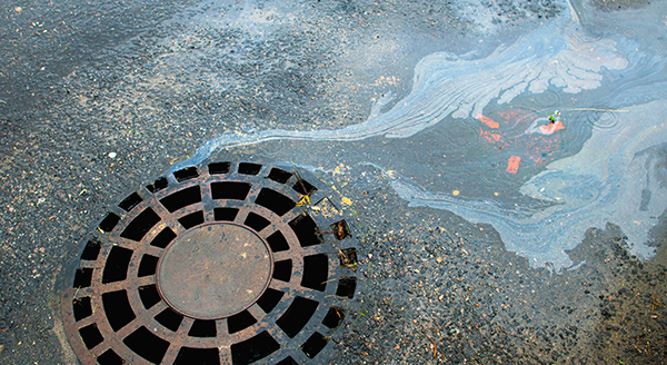 Oily runoff flowing across pavement into a storm drain.